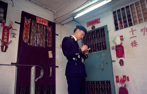 A policeman makes notes  on the 11th floor landing of an apartment block.